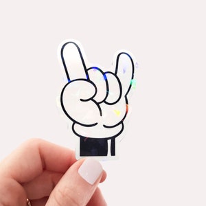 May include: A white hand with black outlines making the 'rock on' hand gesture. The hand is a sticker with a holographic finish.