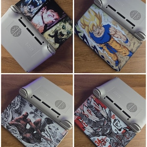 May include: Four gray handheld gaming consoles with different graphic designs on the covers. The designs include anime characters, a superhero, and a stylized illustration. The consoles are on a wooden surface.