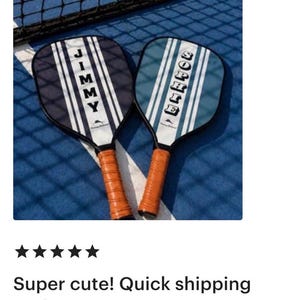 Peut inclure: Deux raquettes de pickleball avec des poign&eacute;es en similicuir marron. La raquette de gauche est bleu fonc&eacute; avec des rayures verticales blanches et le nom JIMMY. Celle de droite est bleu clair avec des rayures blanches et le nom SOPHIE.