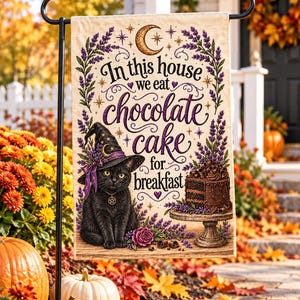 Peut inclure: Un drapeau de jardin rectangulaire illustrant un chat noir portant un chapeau de sorcière violet et un collier pentagramme. Le texte indique In this house we eat chocolate cake for breakfast. Le motif inclut un gâteau au chocolat et de la lavande.