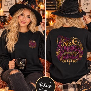 May include: A black crewneck sweatshirt featuring a small graphic on the front left chest and a large, colorful design on the back. The back graphic displays a witch hat, crescent moon, stars, and floral elements with the text No Magic is stronger than sisterhood.