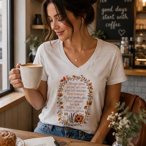 Peut inclure: Un t-shirt col en V gris chiné clair orné d'une couronne graphique aux couleurs automnales. Le motif inclut le texte suivant : Always throw spilled salt over your left shoulder. Keep rosemary by your garden gate. Plant lavender for luck. Fall in love whenever you can.