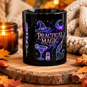 May include: A black ceramic mug featuring a vibrant purple and blue cosmic design with the text "PRACTICAL MAGIC". The graphic includes a witch hat, a crescent moon, a broom, a cat, a cocktail glass, a small bottle, and a sprig of lavender.