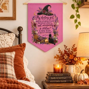 Peut inclure: Une bannière murale en tissu rose ornée d'un chapeau de sorcière noir, d'un balai, d'un chat noir et de fleurs. Le texte indique : My darling girl, when are you going to realize that being normal is not necessarily a virtue? It rather denotes a lack of courage! Aunt Frances.