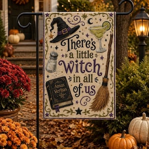 Peut inclure: Un drapeau de jardin rectangulaire avec le texte 'There's a little witch in all of us' en lettres violettes et noires. Les illustrations incluent un chapeau de sorcière noir, un verre à margarita, une salière, un grimoire 'Amas Veritas' et un balai.
