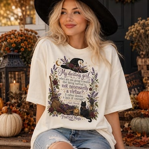 May include: An ivory t-shirt featuring a graphic print of a witch hat, a broom, a black cat, and floral elements. The text reads: My darling girl, when are you going to realize that being normal is not necessarily a virtue? It rather denotes a lack of courage! - Aunt Frances, Practical Magic.