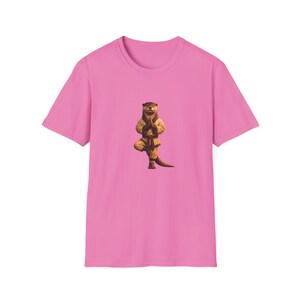 May include: A bright pink short-sleeved t-shirt featuring a centered graphic of an otter wearing a tan martial arts uniform with a dark belt. The otter is depicted in a standing pose with one leg lifted and hands pressed together in a prayer position.