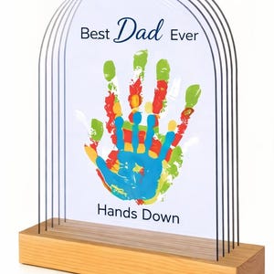 Op de afbeelding: Houten display met een handafdruk in verschillende kleuren. De tekst "Best Dad Ever" en "Hands Down" is afgedrukt. De handafdruk is in blauw, geel, rood en groen.