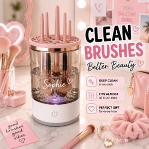 May include: A cylindrical makeup brush cleaner with a white base, a clear water reservoir, and a pink silicone lid featuring multiple slots. The device displays the name Sophie in white script and includes a power button on the front base.