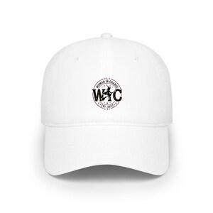 Puede incluir: Gorra de béisbol blanca con un logotipo circular negro que dice "WOMAN IN CHARGE" y "WIC EST. 2023". La gorra tiene una visera curva y una corona estructurada, ideal para la protección solar y el uso informal.