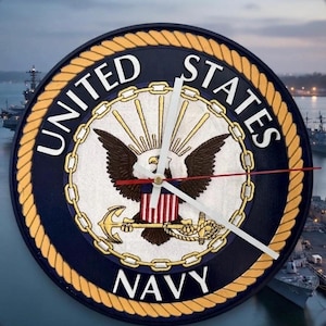 May include: A round wall clock featuring the United States Navy emblem. The design includes a central bald eagle, a shield, and an anchor, surrounded by a gold chain and a rope border. The text UNITED STATES NAVY is printed in white.