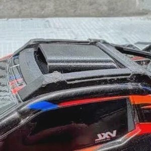 Puede incluir: Primer plano de un coche de juguete negro y rojo con techo texturizado y una rejilla de ventilación visible. El coche presenta detalles en azul y el texto "JXV" en el lateral. La imagen destaca los detalles del diseño del vehículo.