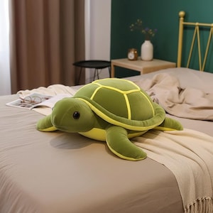 May include: A soft toy turtle in green and yellow colours is lying on a bed. The turtle has a rounded shell with yellow detailing, a soft head, and four flipper-like limbs. The toy is designed to resemble a sea turtle.