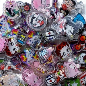 May include: A collection of assorted acrylic charms featuring various cartoon characters, including Betty Boop and Snoopy, alongside medical symbols and text elements like 'it's friday'. The charms are multi-colored, glossy, and flat-backed.
