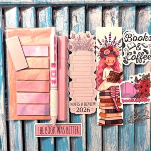 May include: A stationery set featuring a pack of pastel sticky notes, a pink patterned pen, a highlighter, a Notes & Review 2026 notepad, a bookmark with a girl reading on books, two stickers with text Books & Coffee and bookaholic, and paper clips.