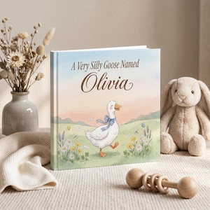 Peut inclure: Un livre pour enfants intitulé "A Very Silly Goose Named Olivia" avec une illustration à l'aquarelle d'une oie portant un nœud bleu. Un lapin en peluche et un hochet en bois sont également dans l'image.