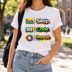 May include: White t-shirt with the text "Sleep. Code. Repeat." in colorful, stylized lettering. The design includes icons of a bed, a laptop with code, and a circular arrow, all with a splash paint effect. The shirt is a casual wear item.