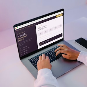 May include: A laptop displaying a website with the text "Welcome Packet" and "A simple, intentional process." The screen shows a form with fields. A smartphone rests beside the laptop. Hands are typing on the keyboard.