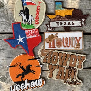 May include: Six embroidered patches featuring Western themes. Designs include a cowboy on a horse with a Texas flag, a Texas state shape with a hat, a Texas-shaped flag with the word HOWDY, a rectangular patch reading HOWDY, a sunset scene with a cowboy and the word yeehaw, and a patch reading HOWDY Y'ALL.
