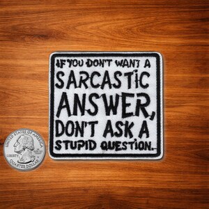 May include: A square, black and white patch with the text "IF YOU DON'T WANT A SARCASTIC ANSWER, DON'T ASK A STUPID QUESTION." A US quarter coin is next to the patch.