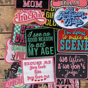 Può includere: Una collezione di toppe in tessuto ricamato con vari slogan e disegni, tra cui frasi come Not the Worst Mom, Living on that Blue Collar Dollar, I see no good reason to act MY AGE e Excuse Me You look like you love me.