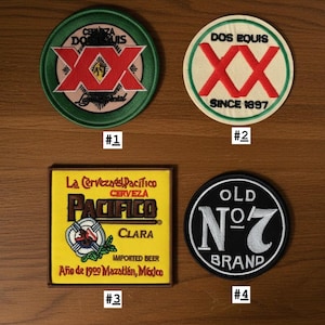 May include: Four embroidered patches: a circular green Dos Equis patch, a circular cream Dos Equis patch with red XX, a square yellow Pacifico Clara patch with brown border, and a circular black Old No. 7 Brand patch with white text and border.