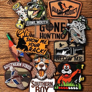 Op de afbeelding: Een verzameling geborduurde patches met jacht- en outdoorthema's, waaronder eenden, honden en jachtpatronen. Tekst bevat "FOWL MOUTH", "QUACK ADDICT", "GONE HUNTING", "SHOW ME YOUR RACK!", "BLOW ME", "SOUTHERN VIBES" en "SOUTHERN BOY".