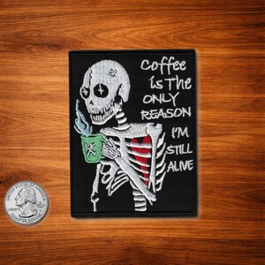 May include: Black embroidered patch with a skeleton design holding a green coffee cup. The text on the patch says "Coffee is the only reason I'm still alive."