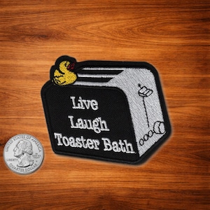 May include: Embroidered patch with a black background and the words "Live Laugh Toaster Bath" in white. A yellow duck with a red bow is at the top. A quarter coin is next to the patch.