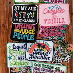 Puede incluir: Una colección de parches bordados rectangulares y con formas que presentan diseños coloridos y textos relacionados con cócteles y bebidas, incluyendo frases como Spicy Marg Queen, Day Drinker, At My Age I Need Glasses, Cowgirls Tequila, Drink and Judge People, Beer and Sunshine y One Tequila Two Tequila Three Tequila Floor.