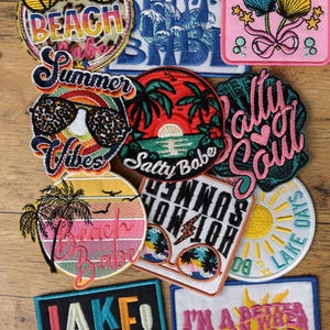 May include: A collection of embroidered fabric patches featuring summer and beach themes. Designs include sunglasses, palm trees, seashells, and suns with text such as Beach Babe, Summer Vibes, Salty Soul, Lake Days, Lake Mode, and I'm a better person when I'm tan.