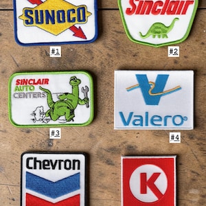 May include: Six embroidered patches featuring vintage gas station logos. Patch 1: Sunoco. Patch 2: Sinclair with a green dinosaur. Patch 3: Sinclair Auto Centers with a green dinosaur holding a wrench. Patch 4: Valero. Patch 5: Chevron. Patch 6: Circle K.