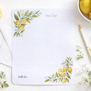 Peut inclure: Papeterie blanche lignée avec des illustrations de citrons et de feuilles à l'aquarelle. La papeterie porte les mentions "From Sarah" et "With love". Une enveloppe blanche, des trombones dorés, un stylo et des citrons sont également présents.