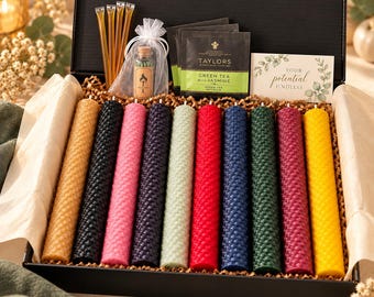 May include: A black gift box containing ten cylindrical beeswax candles with a honeycomb texture in yellow, black, pink, purple, light green, red, blue, dark green, magenta, and gold. Includes honey sticks, matches in a glass bottle, Taylors Green Tea with Jasmine tea bags, and a card reading Your potential is endless.