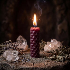 May include: A deep burgundy pillar candle with a textured honeycomb pattern is lit, emitting a bright flame and thin wisp of smoke. The candle is surrounded by clear quartz crystals, dried lavender sprigs, and scattered herbs.