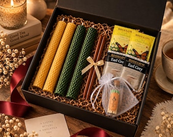 May include: A black gift box containing two yellow honeycomb beeswax candles, two green honeycomb beeswax candles, two brown taper candles tied with a ribbon, two Bigelow Cozy Chamomile tea bags, two Bigelow Earl Grey tea bags, and a small glass bottle of matches.