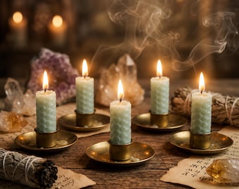 May include: Five light green honeycomb-textured pillar candles with lit wicks, each resting in a small brass candle holder. The candles are arranged on a wooden surface alongside several raw crystals and bundles of dried sage on parchment paper.