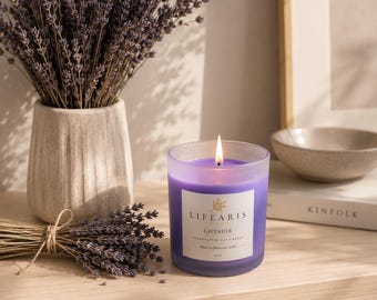 May include: A lit purple soy candle in a frosted glass jar with a white label reading "LIFEARIS LAVENDER HANDCRAFTED SOY CANDLE Made in Missouri, USA 8 OZ". The candle is accompanied by a bundle of dried lavender stems and a textured ceramic vase.