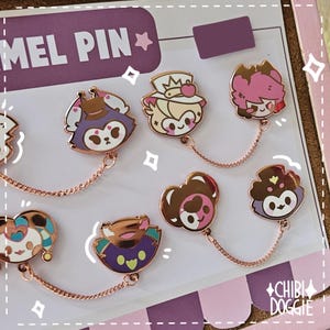 Puede incluir: Una colección de pines de esmalte con varias cabezas de personajes de dibujos animados, cada par conectado por una fina cadena de metal en oro rosa. Los pines muestran diversos colores, incluyendo morado, rosa, marrón y verde azulado.
