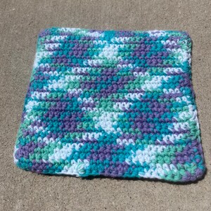 May include: A square crochet washcloth featuring a variegated yarn pattern in shades of purple, teal, light green, and white. The textile is constructed with a dense, uniform stitch pattern, creating a textured surface across the entire square.