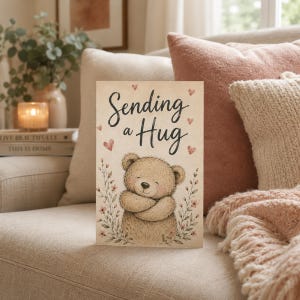 Może przedstawiać: Prostokątna kartka okolicznościowa z brązowym pluszowym misiem ze skrzyżowanymi ramionami. Napis Sending a Hug wykonano czarną czcionką. Wzór zawiera małe różowe serduszka i delikatne gałązki kwiatowe na jasnobeżowym tle.
