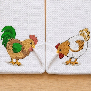 Può includere: Due strofinacci da cucina bianchi a trama a nido d'ape con disegni ricamati di gallo e gallina. Il gallo è marrone, verde e giallo, mentre la gallina è bianca e marrone. Entrambi hanno creste rosse e becchi gialli. Gli asciugamani sono esposti su una superficie marrone chiaro.