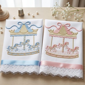 Puede incluir: Dos mantas bordadas blancas para bebé. Una presenta un diseño de carrusel azul con una cinta azul y un ribete de encaje. La otra tiene un diseño de carrusel rosa con una cinta rosa y un ribete de encaje. El diseño del carrusel incluye caballos.
