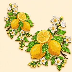 Op de afbeelding: Twee geborduurde patches met gele citroenen, groene bladeren en witte citrusbloesems. Het ontwerp bevat hele citroenen en gehalveerde citroenschijfjes met gedetailleerd stikwerk, gerangschikt op takken met kleine knoppen en vijfbladige bloemen.