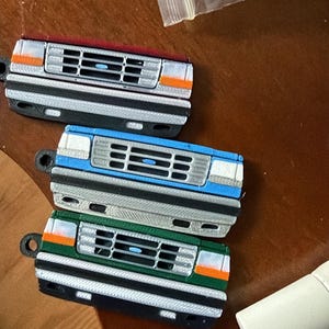 Può includere: Tre portachiavi con la parte anteriore di un camion in miniatura, rossi, blu e verdi. Ogni portachiavi presenta una griglia, fari e paraurti dettagliati. Realizzati in plastica dura, assomigliano a un classico pick-up.