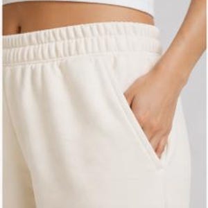 Puede incluir: Pantalones de ch&aacute;ndal color crema con cintura el&aacute;stica y bolsillos. La imagen muestra un primer plano de la cintura y la zona de los bolsillos, con una mano dentro de uno de los bolsillos. La tela parece suave y c&oacute;moda.