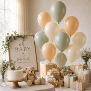 May include: A baby shower display featuring a sign that reads oh BABY WELCOME TO Baby Smith's BABY SHOWER, a white cake, a tan teddy bear, and a cluster of sage green, cream, and peach balloons tied with gold strings near gift boxes.
