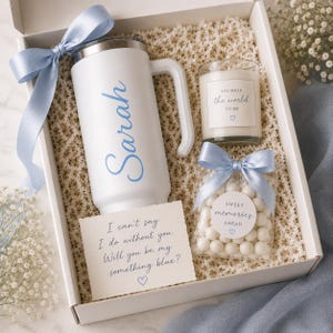 Könnte beinhalten: Eine weiße Geschenkbox mit einem weißen Becher mit dem Namen Sarah in blauer Schrift, einer Kerze mit der Aufschrift You mean the world to me, einer Tüte weißer Bonbons mit der Aufschrift Sweet memories ahead und einer Karte mit dem Text I can't say.