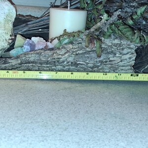 Puede incluir: Un centro de mesa decorativo de madera con textura de corteza natural, con una vela blanca, flores secas y cristales de colores. El centro de mesa mide aproximadamente 46 cm de largo, medido con una cinta m&eacute;trica amarilla.