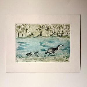 May include: An etched print of a bird family walking near a body of water. The artwork features a large bird leading two smaller birds across a grassy area. Trees and a body of water are in the background. The print is in shades of green, blue, and black.